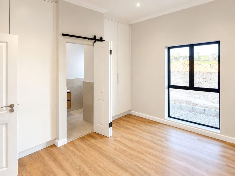 A bright, modern bedroom featuring built-in cupboards, laminate flooring, and an en-suite bathroom access via a sliding barn door.
