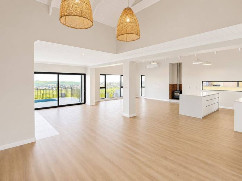 Spacious open-plan living and kitchen area featuring vaulted ceilings, modern laminate flooring, a central kitchen island, and a cozy wood-burning fireplace.