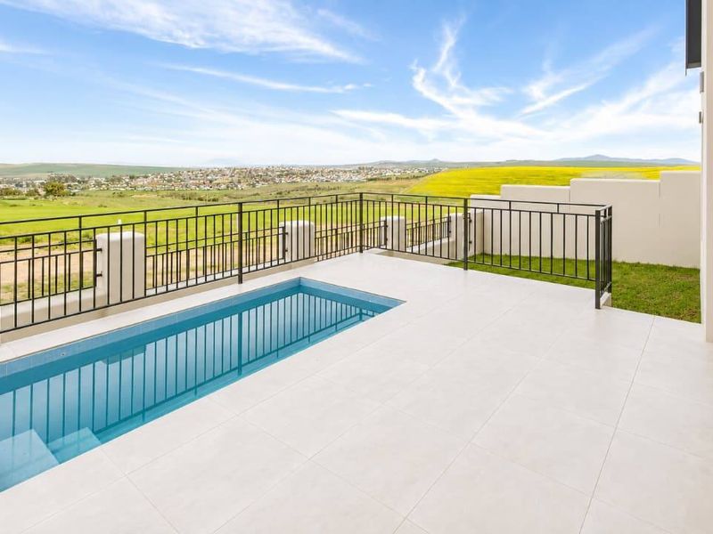 A modern outdoor patio featuring a sleek plunge pool, tiled flooring, and a metal balustrade overlooking a scenic landscape.