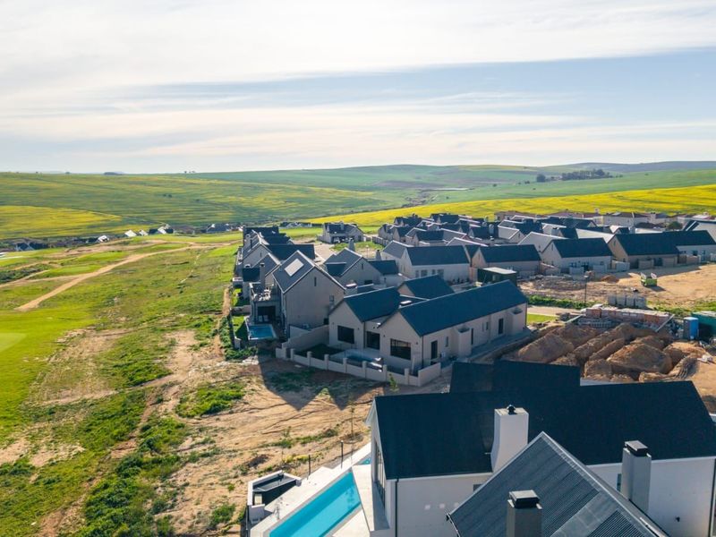 Aerial view of a modern residential estate featuring contemporary homes with pitched roofs, swimming pools, and surrounding landscaped golf course grounds.