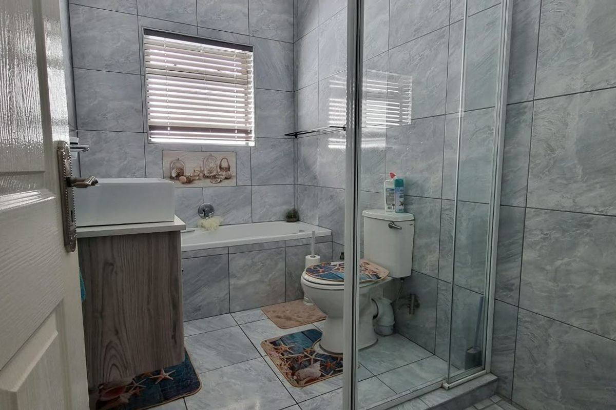 A modern bathroom featuring grey tiled walls and floors, a built-in bathtub, a separate glass-enclosed shower, and a vanity with a vessel sink.