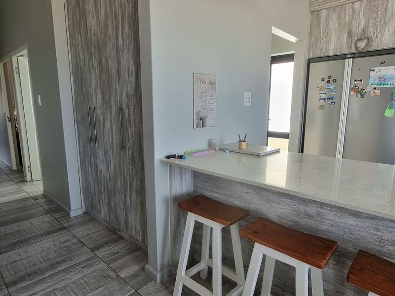 Open plan kitchen area featuring modern wood-look cabinetry, stone countertops, a breakfast bar, and subway tile backsplash, seamlessly connecting to the hallway.