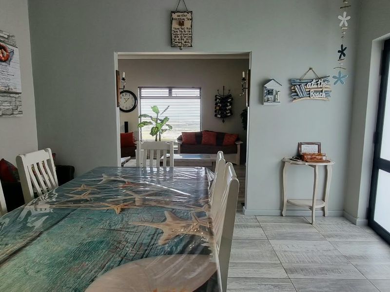 Dining area featuring light-toned tiled flooring and a glass panel door leading to the exterior, with an open-plan flow into the adjacent living space.
