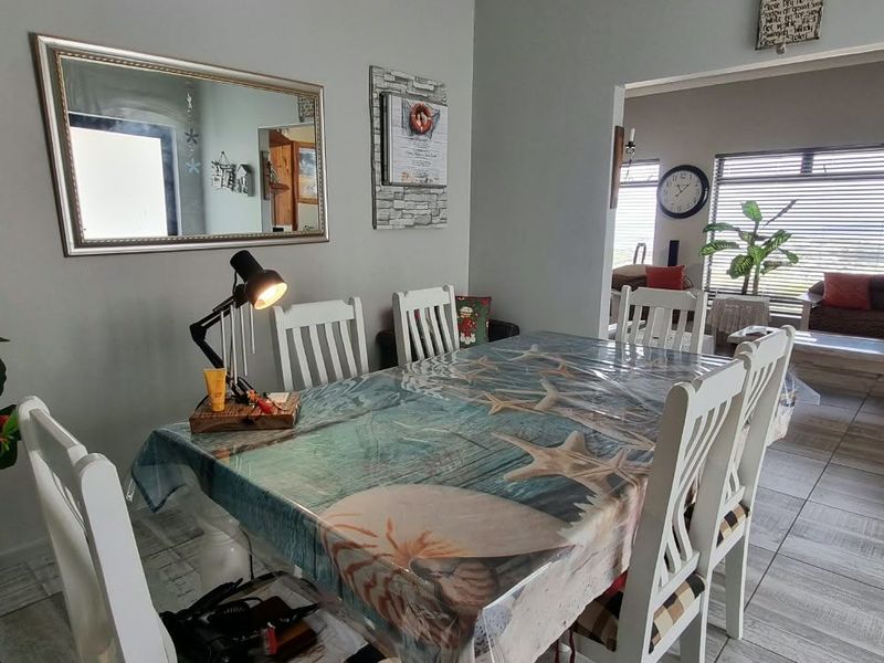 Open plan dining area featuring light-toned tiled flooring and an archway leading into an adjacent living space with large windows.