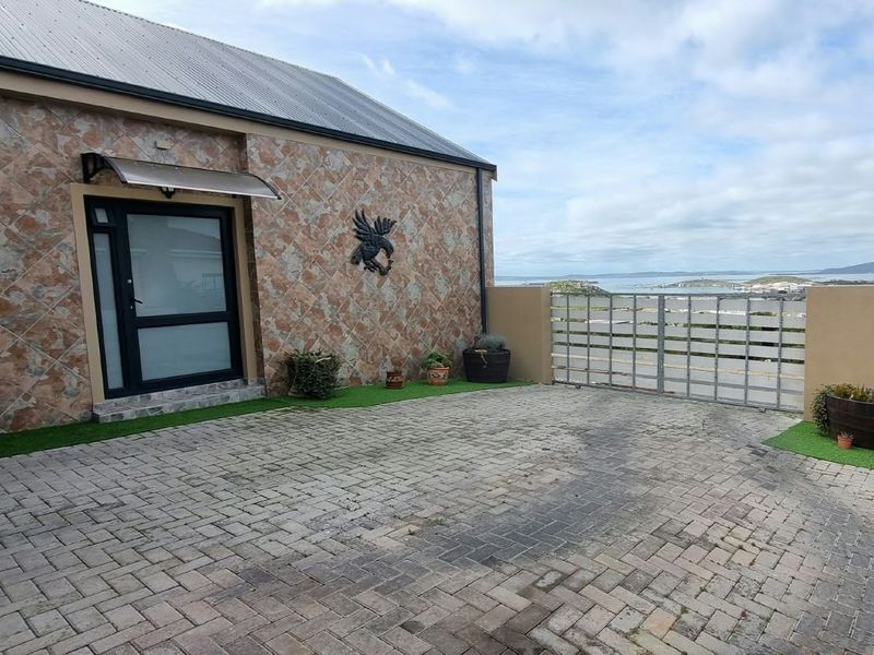 Front entrance area featuring a paved driveway, stone-clad exterior wall, and a metal security gate with coastal views.