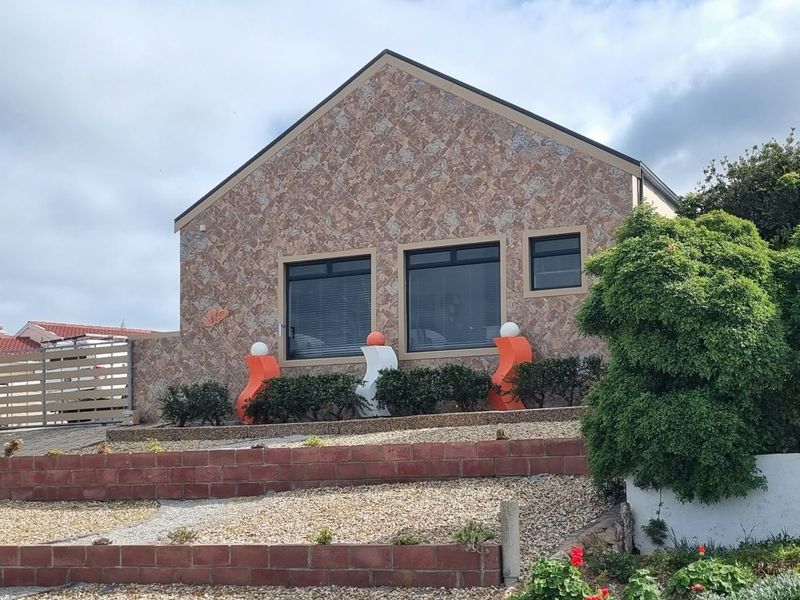 Front elevation of a house featuring stone cladding, aluminium windows, and tiered brick retaining walls with gravel landscaping.