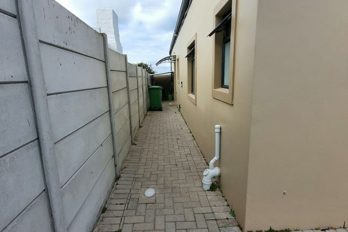 A narrow paved side passage along the exterior of the house, featuring a precast concrete boundary wall and external plumbing fixtures.