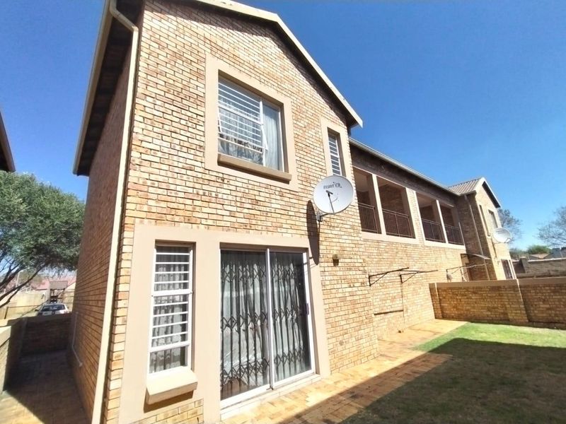 Rear view of the townhouse featuring a face brick facade, a paved patio area, and an upper-level balcony overlooking the private garden.
