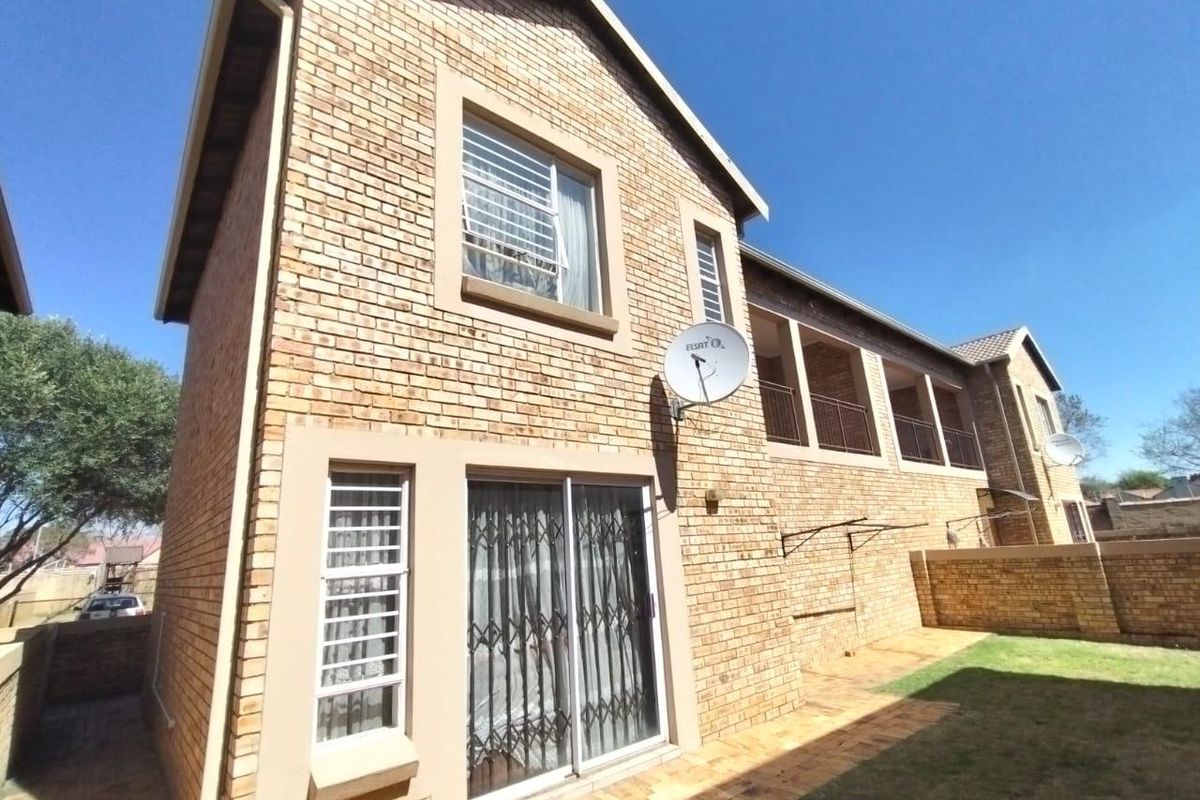 Rear view of the townhouse featuring a face brick facade, a paved patio area, and an upper-level balcony overlooking the private garden.