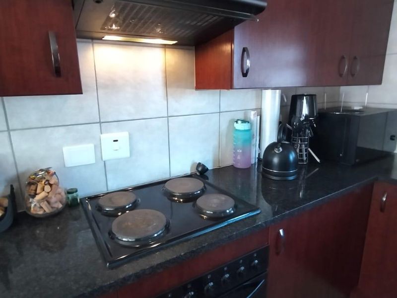 A functional kitchen featuring dark wood cabinetry, granite countertops, a built-in electric oven and hob, and a tiled backsplash.