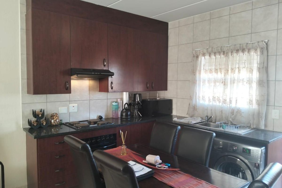 Functional kitchen featuring dark wood cabinetry, granite countertops, built-in oven and hob, and integrated laundry plumbing, offering a practical layout for daily use.