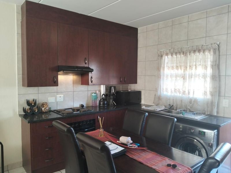 Functional kitchen featuring dark wood cabinetry, granite countertops, built-in oven and hob, and integrated laundry plumbing, offering a practical layout for daily use.