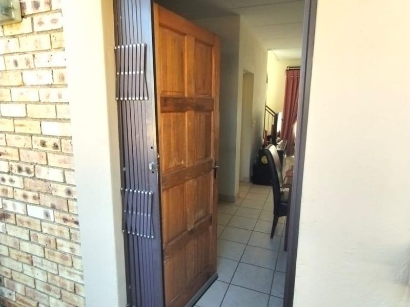 Main entrance featuring a security gate, solid timber door, and tiled flooring leading into the interior living space.