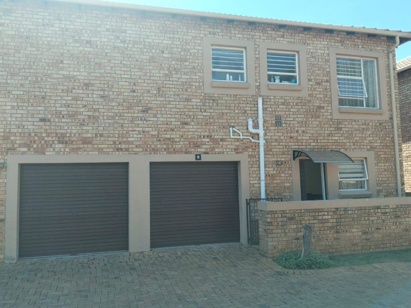 Front elevation of a double-story townhouse featuring a double garage, brick facade, and paved driveway access.