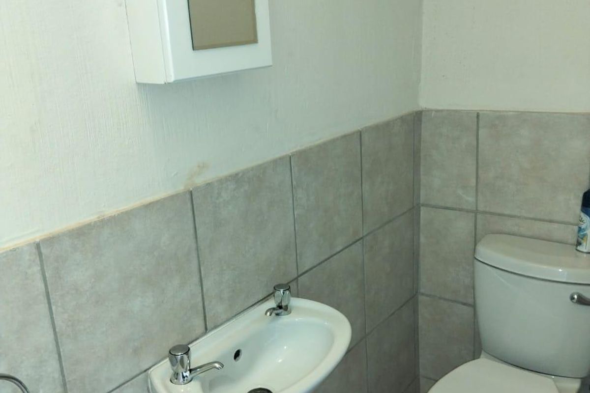 A compact bathroom featuring a wall-mounted basin, toilet, and tiled finishes, requiring minor cosmetic updates and plumbing concealment.