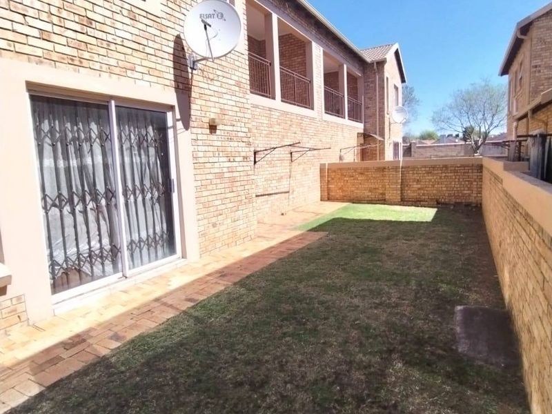 Rear exterior view of the townhouse featuring a private garden, brick boundary walls, a paved walkway, and an upper-level balcony.