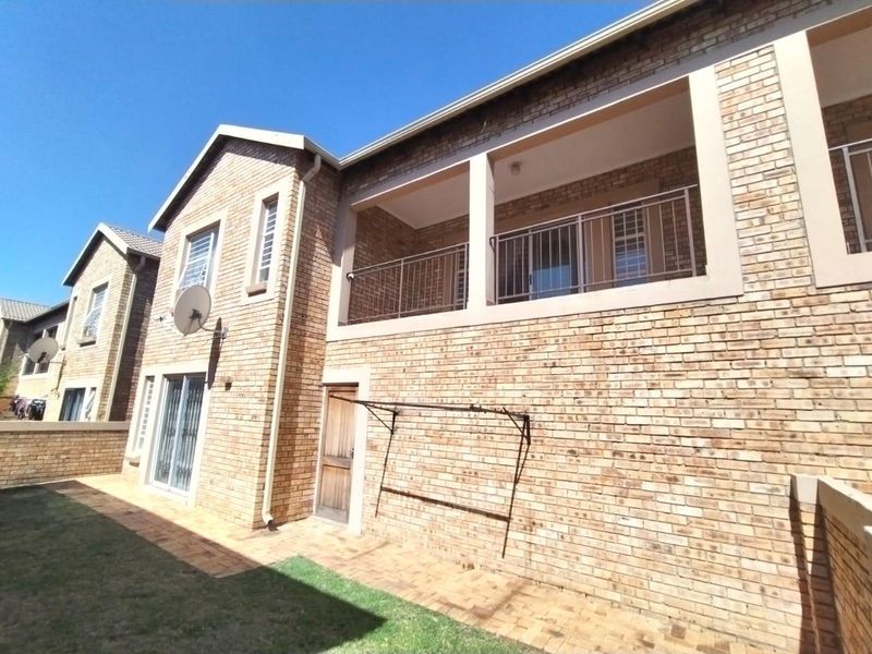 Rear view of a face brick townhouse featuring a paved patio area, a private upper-level balcony with metal railings, and a wall-mounted washing line.
