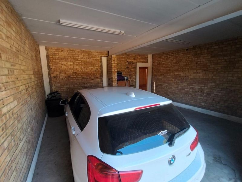A functional garage space featuring exposed brick walls, concrete flooring, and overhead fluorescent lighting, providing secure parking or additional storage capacity.