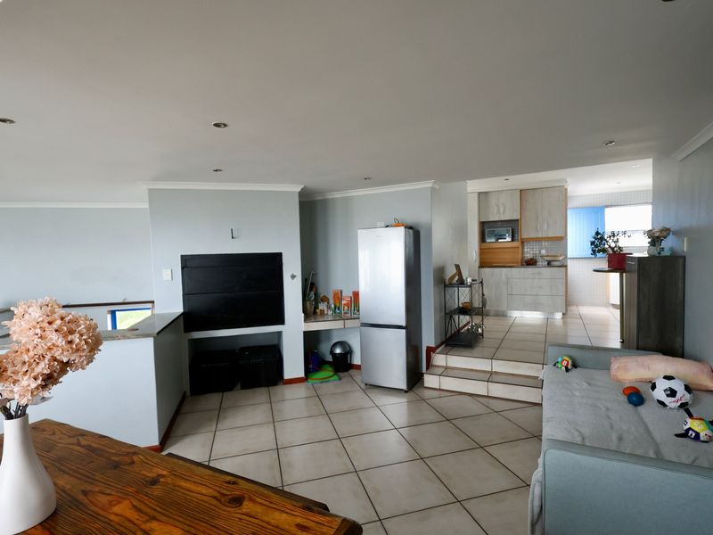 Open plan living area featuring tiled flooring, a built-in fireplace, and a raised kitchen area with modern cabinetry.