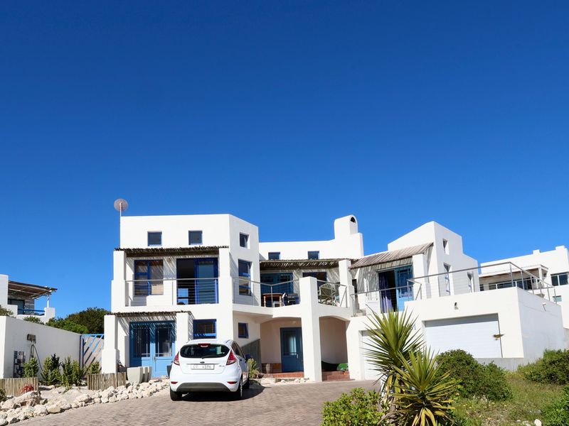A modern multi-level residential property featuring a paved driveway, double garage, and multiple balconies with blue accents under a clear sky.