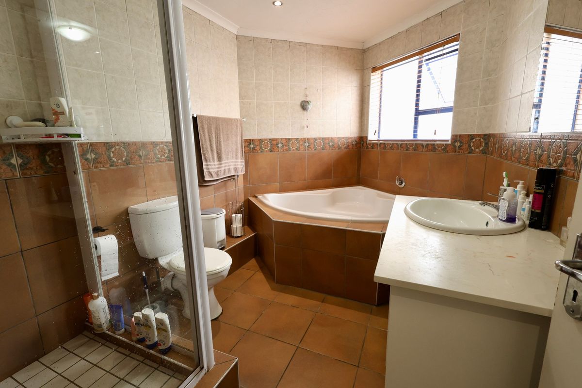 A functional bathroom featuring a corner bathtub, separate shower enclosure, and a vanity basin with built-in cabinetry, finished with neutral wall and floor tiles.