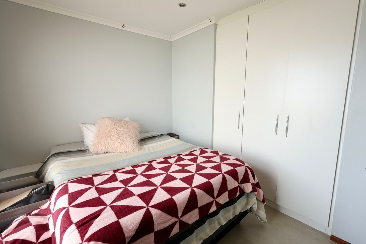 A well-maintained bedroom featuring neutral walls, tiled flooring, and ample storage provided by a large, white built-in wardrobe.