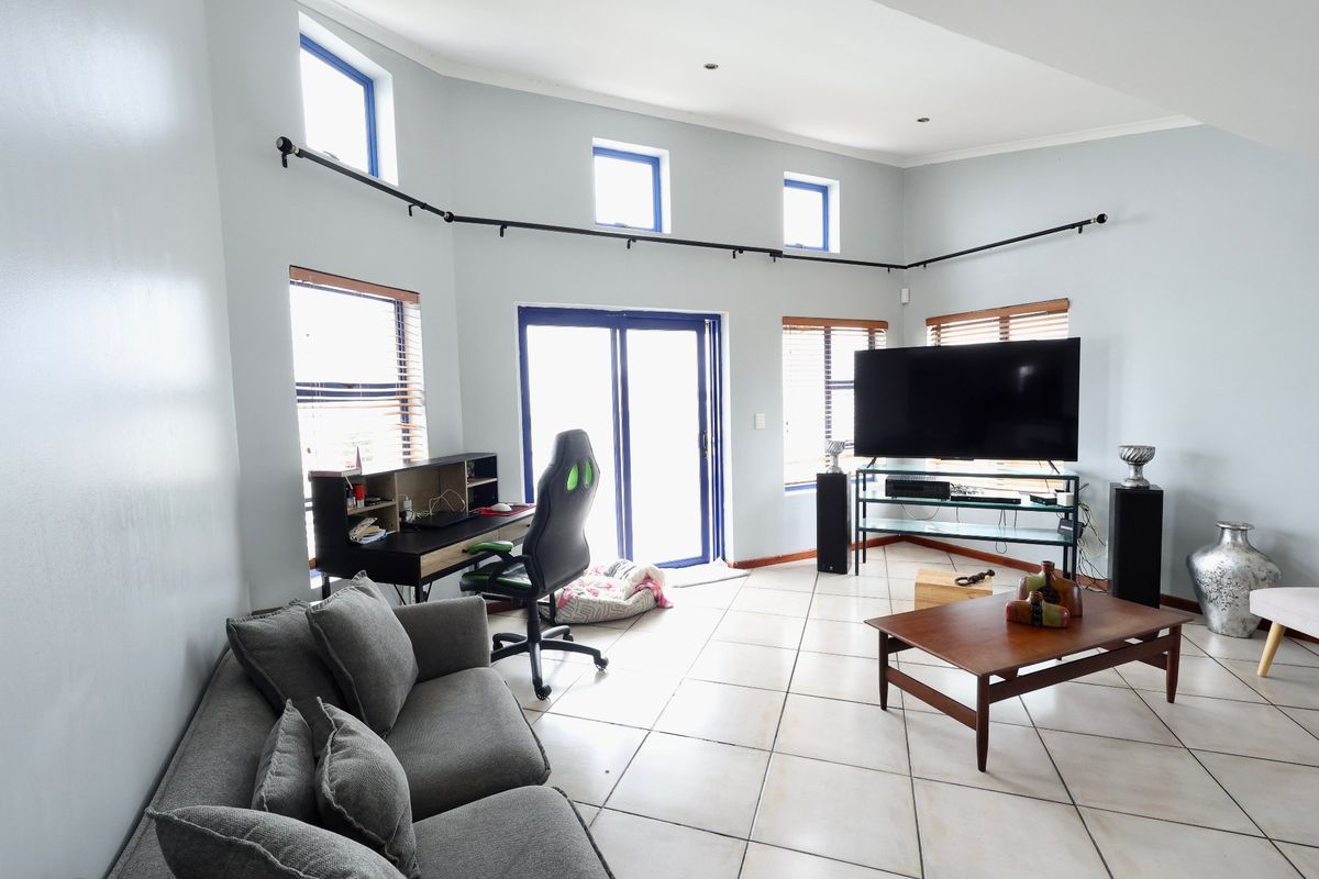 Spacious living room featuring tiled flooring, track lighting, and multiple windows providing natural light, with direct access to an outdoor area via sliding doors.