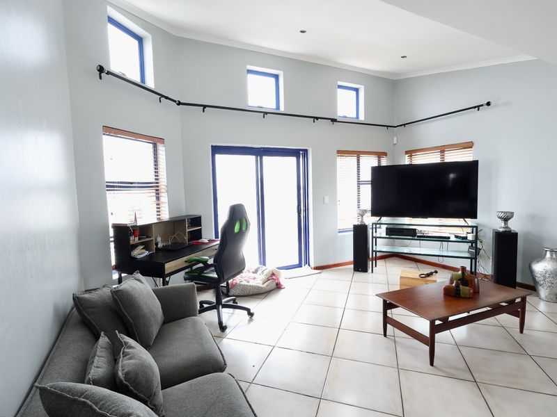 Spacious living room featuring tiled flooring, track lighting, and multiple windows providing natural light, with direct access to an outdoor area via sliding doors.