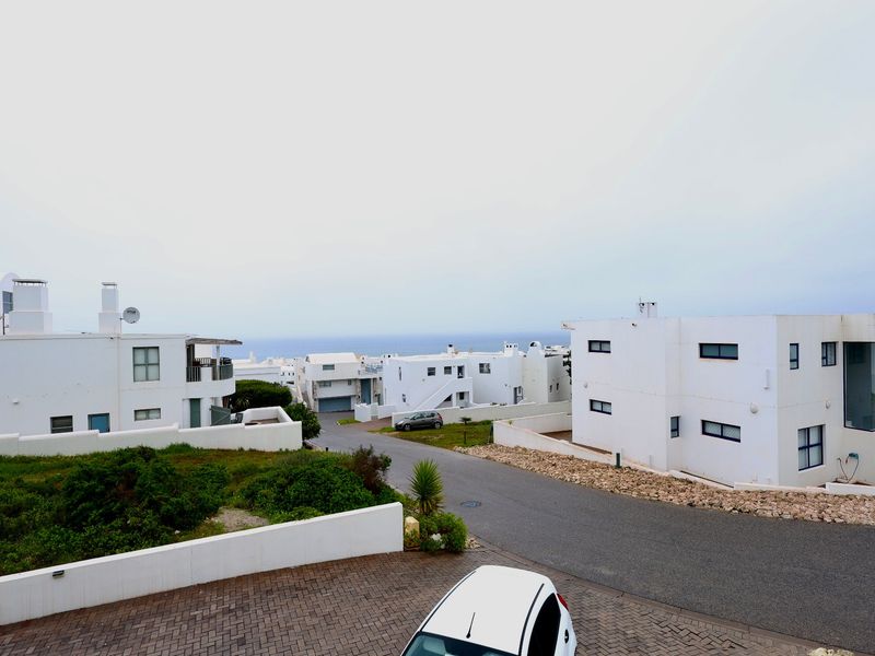 Elevated view overlooking the residential estate street with white coastal-style architecture and distant ocean horizon.