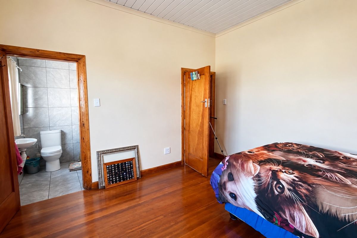 A bedroom featuring polished hardwood flooring, timber door frames, and an adjoining en-suite bathroom with tiled finishes.