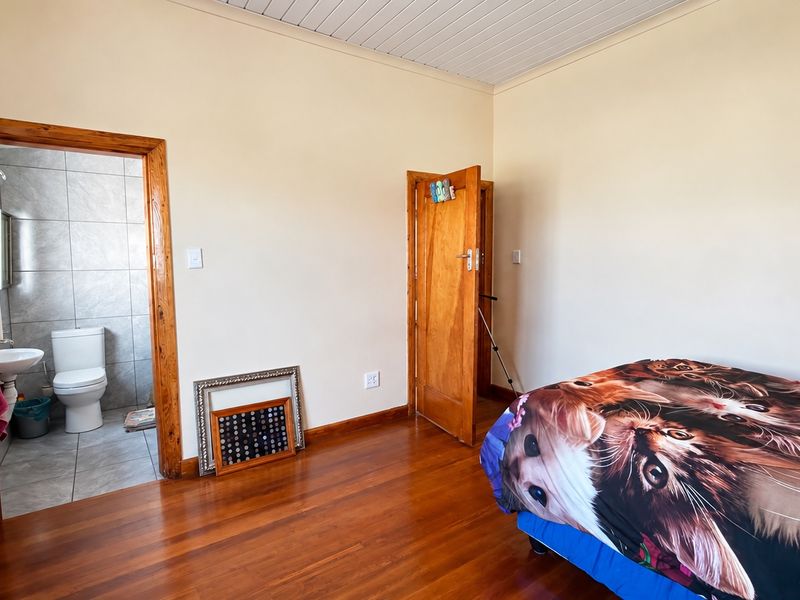 A bedroom featuring polished hardwood flooring, timber door frames, and an adjoining en-suite bathroom with tiled finishes.