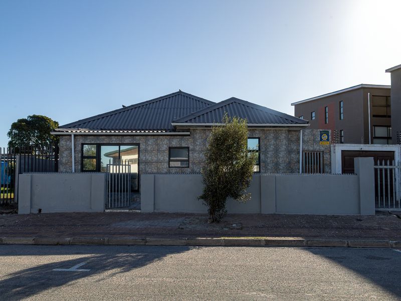 Front elevation of a single-story house featuring stone cladding, a metal roof, and a secure perimeter wall with metal fencing.