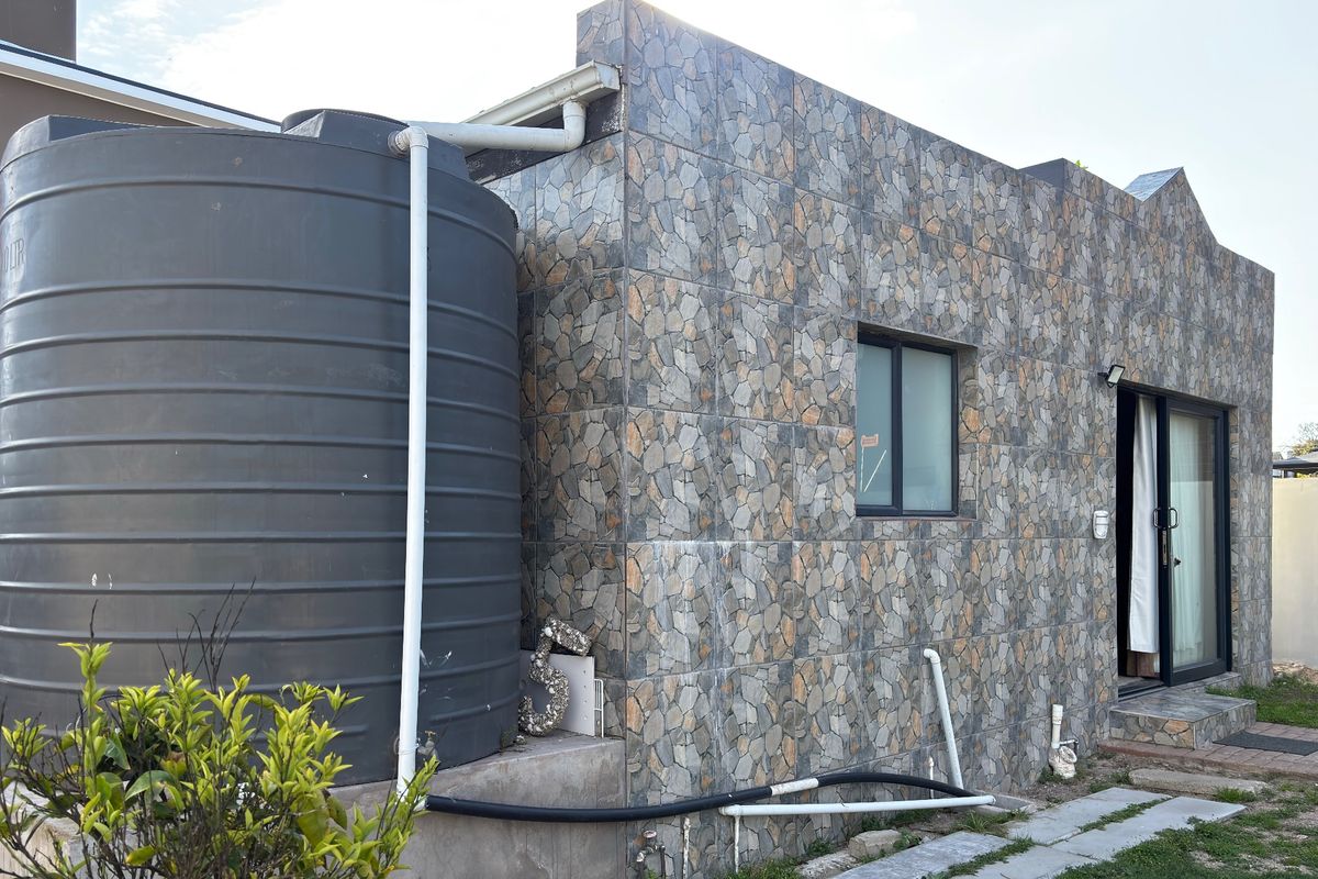 Rear exterior view of the property featuring a stone-clad facade, large water storage tank, and sliding glass door access.