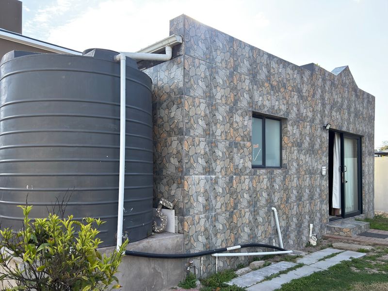 Rear exterior view of the property featuring a stone-clad facade, large water storage tank, and sliding glass door access.