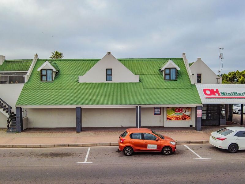 Front elevation of a commercial retail building featuring a green corrugated roof, dormer windows, and dedicated street-level parking.