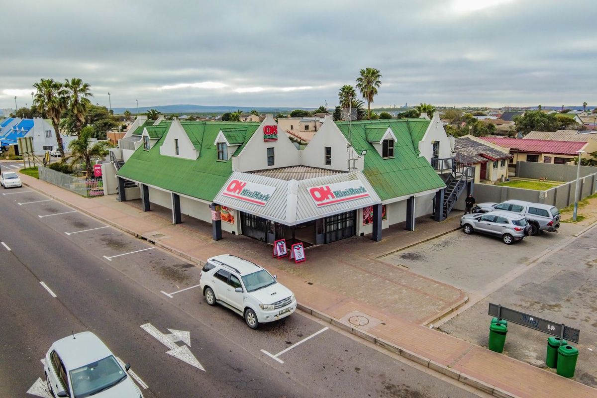 Aerial view of a commercial corner property featuring a green metal roof, paved parking area, and external access staircase.