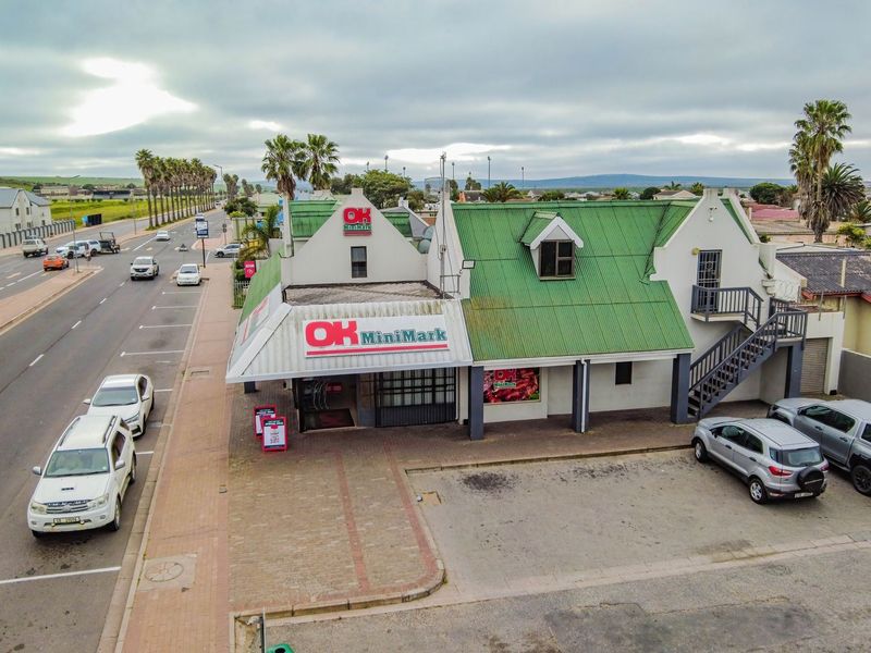Aerial view of a commercial property featuring a green corrugated roof, external staircase, and paved parking area situated along a main road.