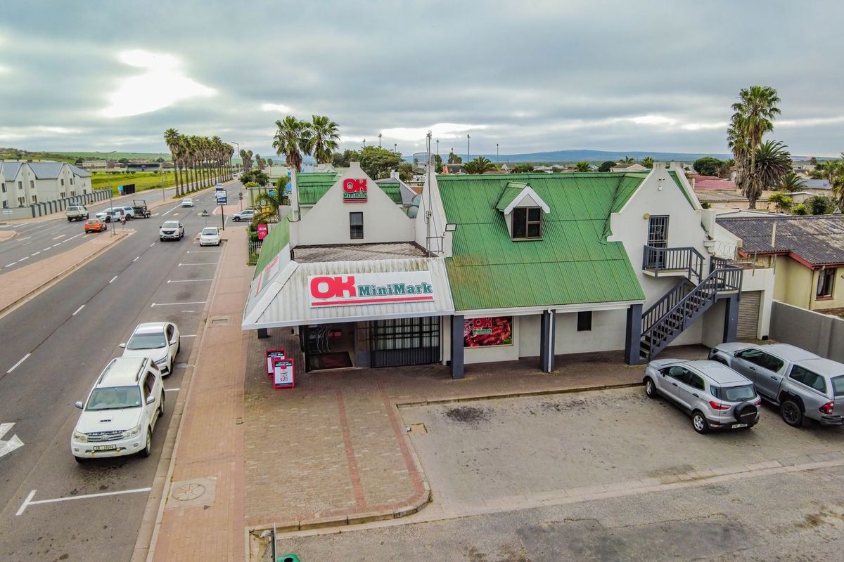 Aerial view of a commercial property featuring a green corrugated roof, external staircase, and paved parking area situated along a main road.
