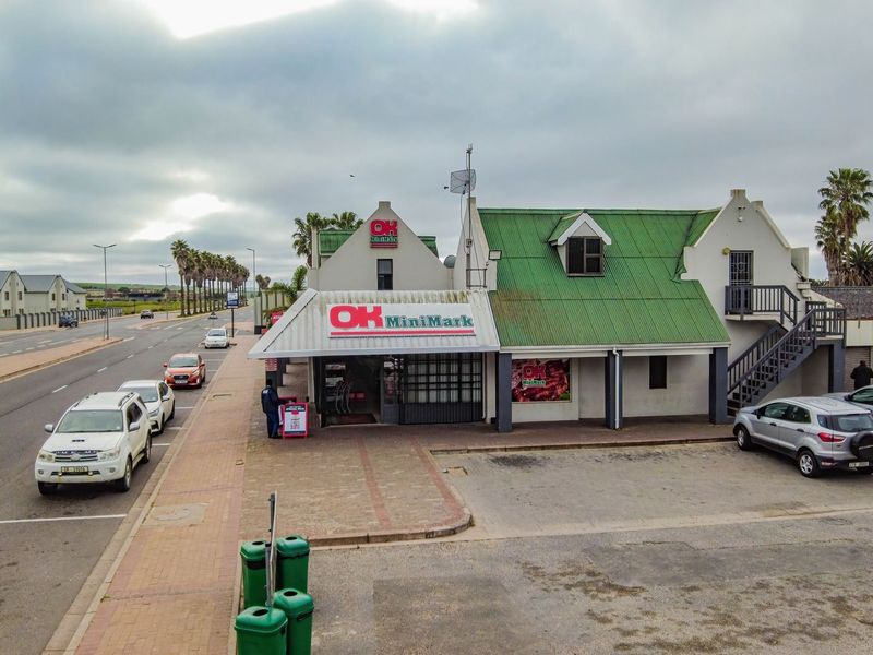 Aerial view of a commercial retail property featuring a prominent storefront, green corrugated roof, external staircase, and dedicated paved parking area.