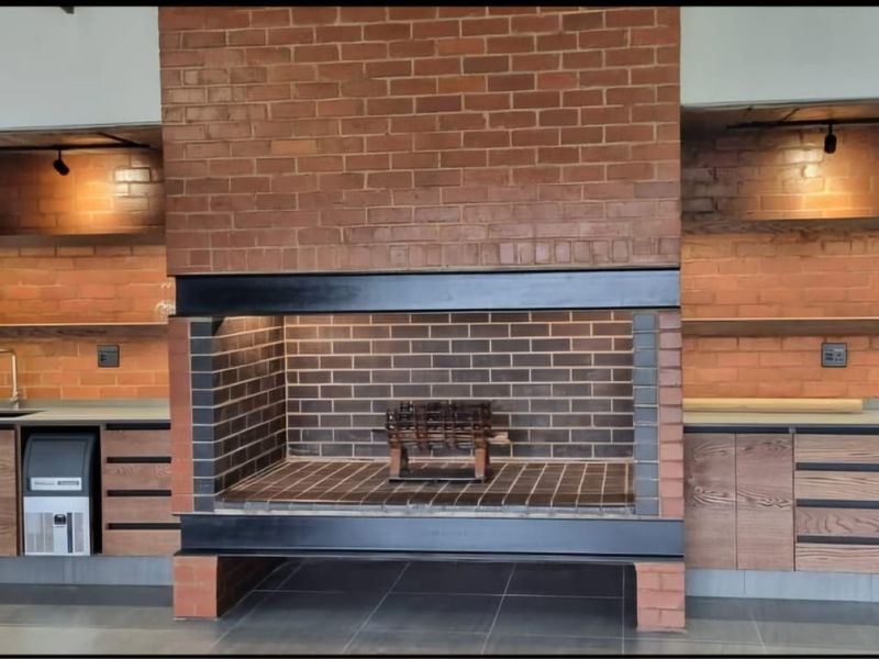 A modern living area featuring a prominent central brick fireplace, built-in cabinetry with floating shelves, and sleek tiled flooring.