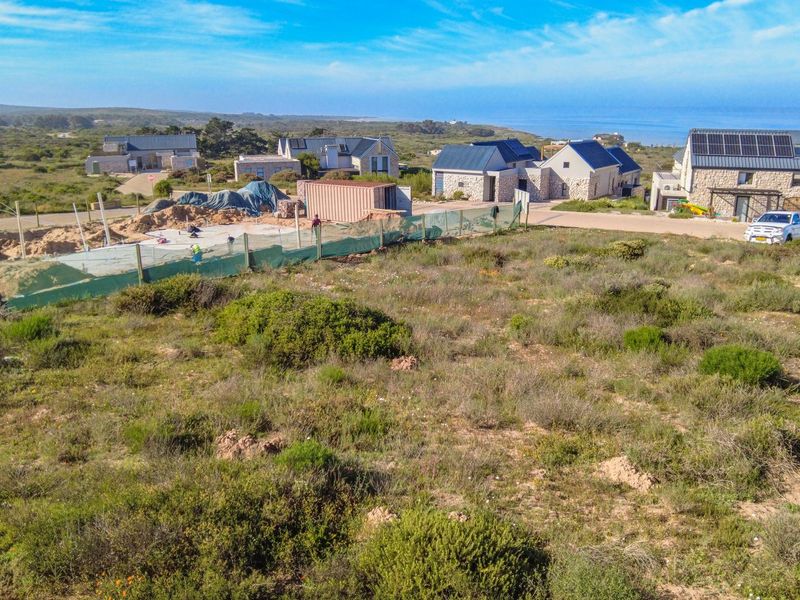 An aerial view of a vacant residential plot in a coastal estate, showing surrounding development and natural vegetation.