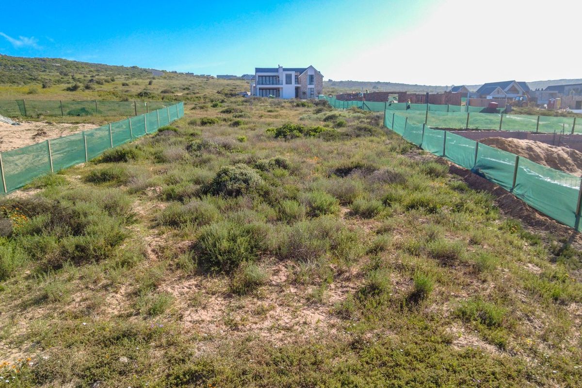 A vacant residential plot featuring natural vegetation, enclosed by perimeter fencing with green shade cloth screening in a developing estate.