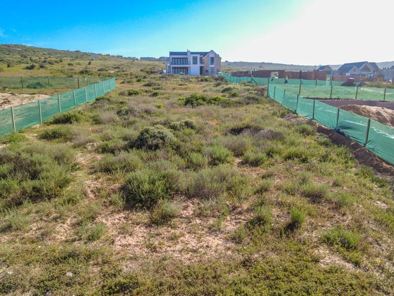 A vacant residential plot featuring natural vegetation, enclosed by perimeter fencing with green shade cloth screening in a developing estate.