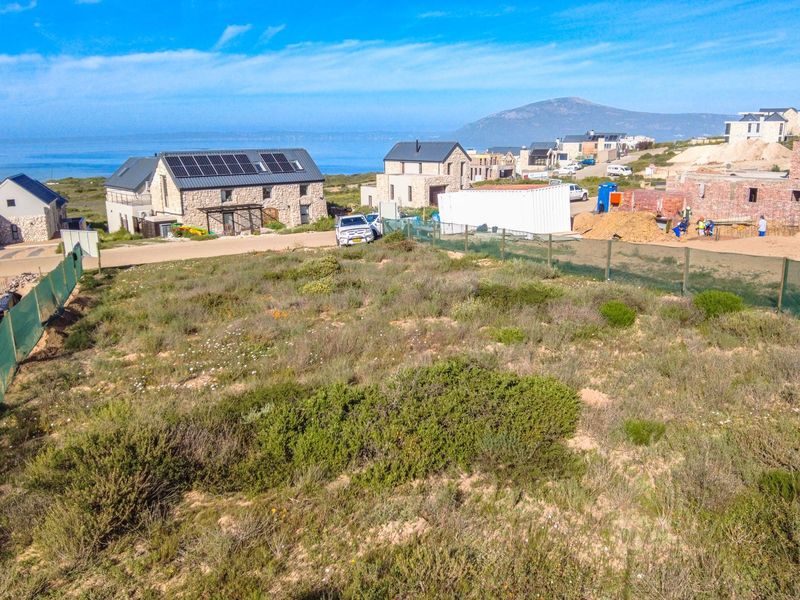 Aerial view of a vacant residential plot in a coastal development, showcasing surrounding neighborhood construction and scenic landscape.