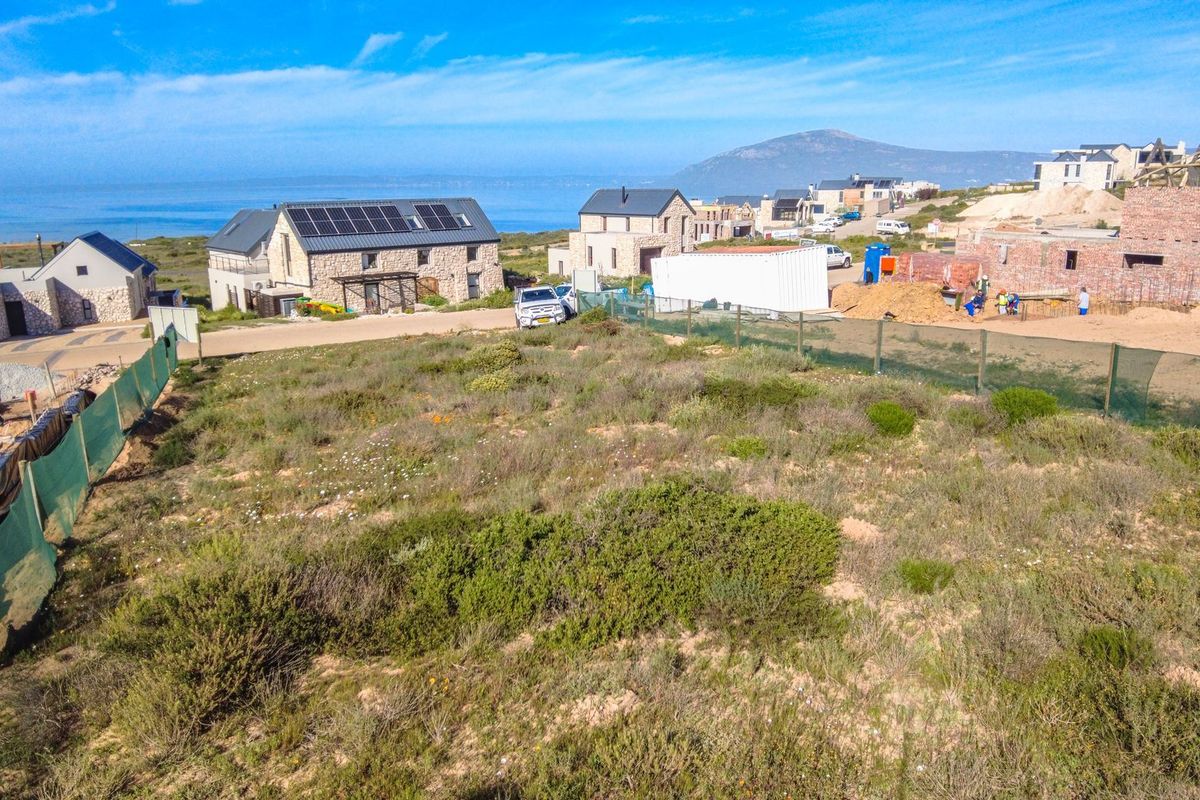 Aerial view of a vacant residential plot in a coastal development, showcasing surrounding neighborhood construction and scenic landscape.