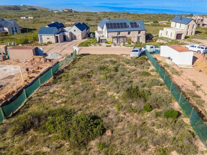 An aerial view of a vacant residential plot featuring perimeter fencing, situated in a coastal estate with surrounding development.