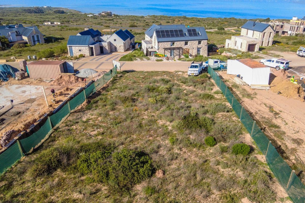 An aerial view of a vacant residential plot featuring perimeter fencing, situated in a coastal estate with surrounding development.