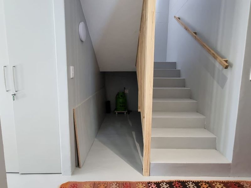 A clean, modern hallway featuring a staircase with a wooden handrail and a convenient under-stair storage space with a built-in cupboard.
