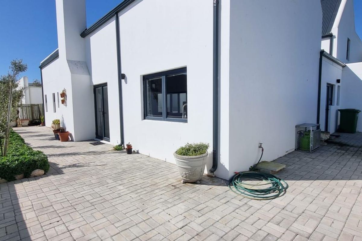 A well-maintained rear exterior view featuring a paved patio area, white rendered walls, and modern dark aluminium window frames.