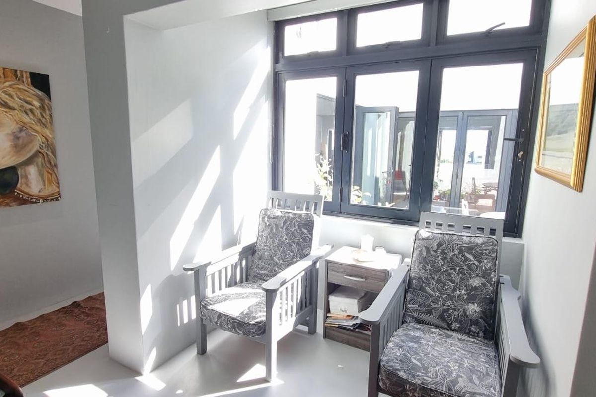 A bright, sunlit seating area featuring modern dark-framed windows and neutral tiled flooring, creating a comfortable and inviting space.